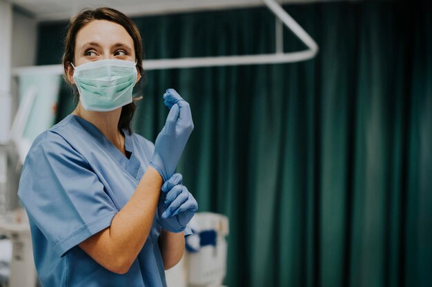 Infirmière debout, porte un masque, porte des gants, femme, tenue bleu, rideau vert